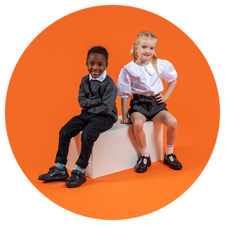 School boy and girl sat on a white box with an orange background, wearing Hush Puppies school shoes
