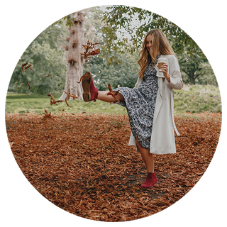 Woman kicking up autumn leaves in a park, wearing a pair of red Hush Puppies boots