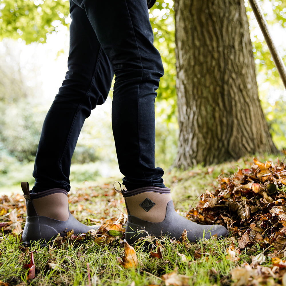 Person stood on grass with fallen autumn leaves around them, wearing a pair of Muck Boots Muckster boots
